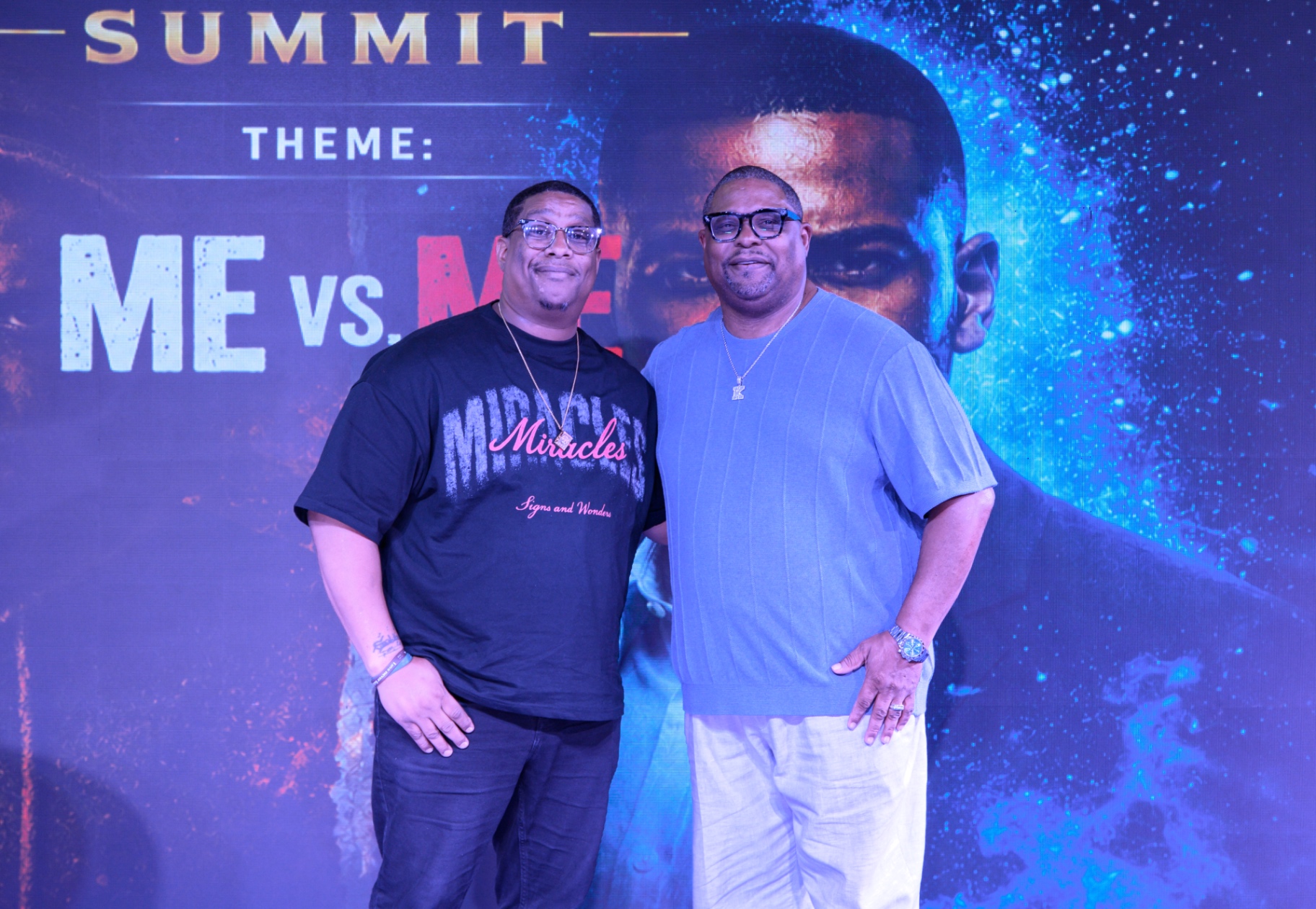 Two men speaking together on the What's Up King stage before the Me vs. Me backdrop